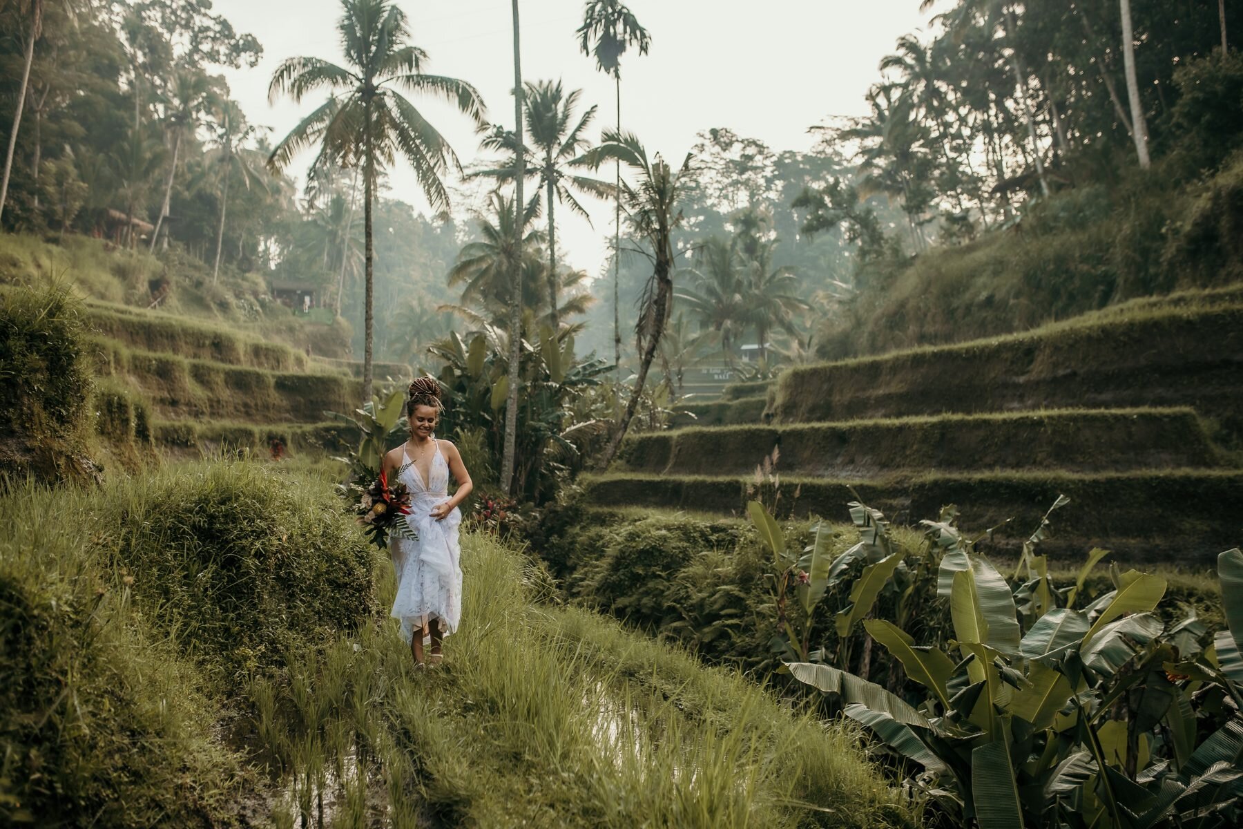 Bride in a white dress walks through terraced rice fields during her Bali elopement