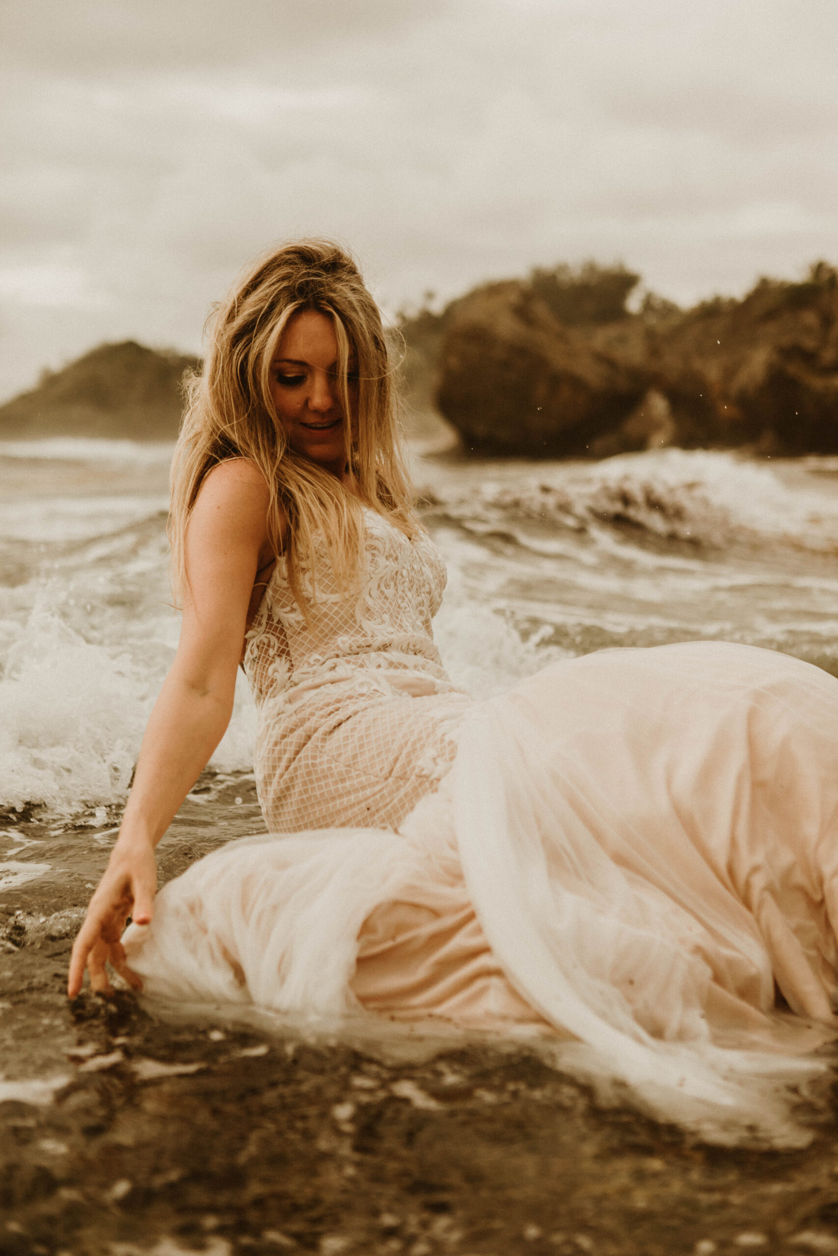 bride sitting in the rolling surf letting the waves wash over her dress after choosing to elope in Barbados