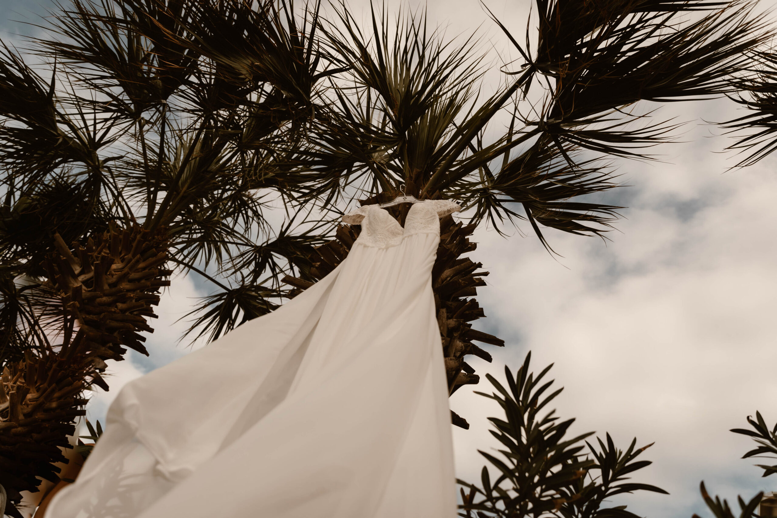 White wedding dress blowing in the Gulf breeze under palm trees in Destin