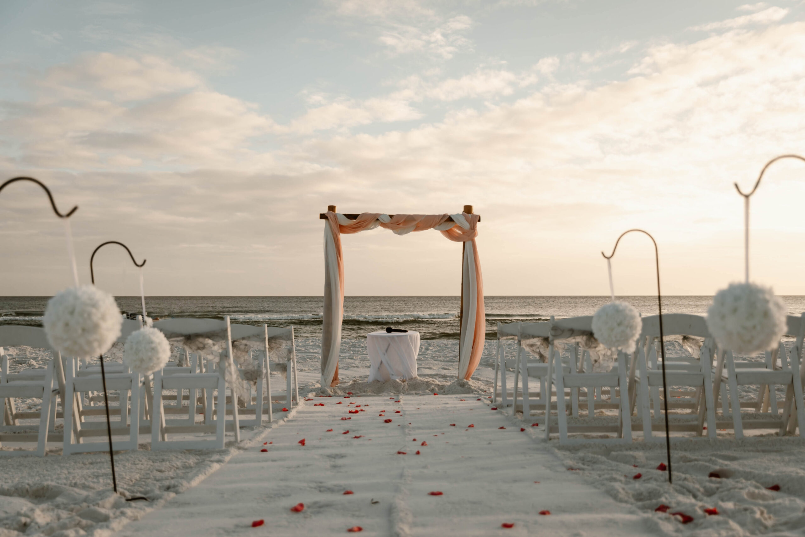 Draped wedding arbor and white chairs set up on the white sand at Pompano Beach in Destin