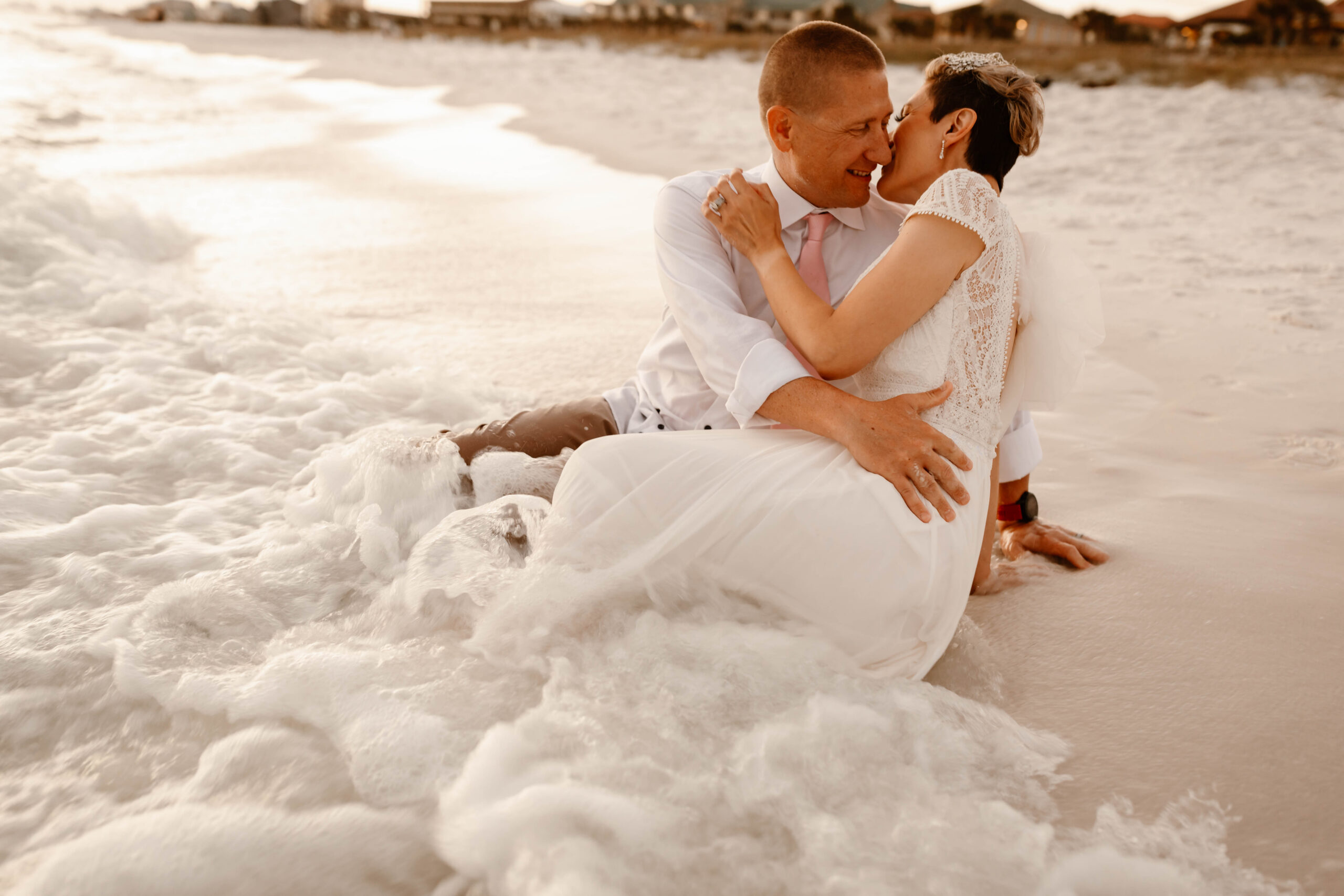 Couple sitting in the sea foam on the beach after their Destin vow renewal