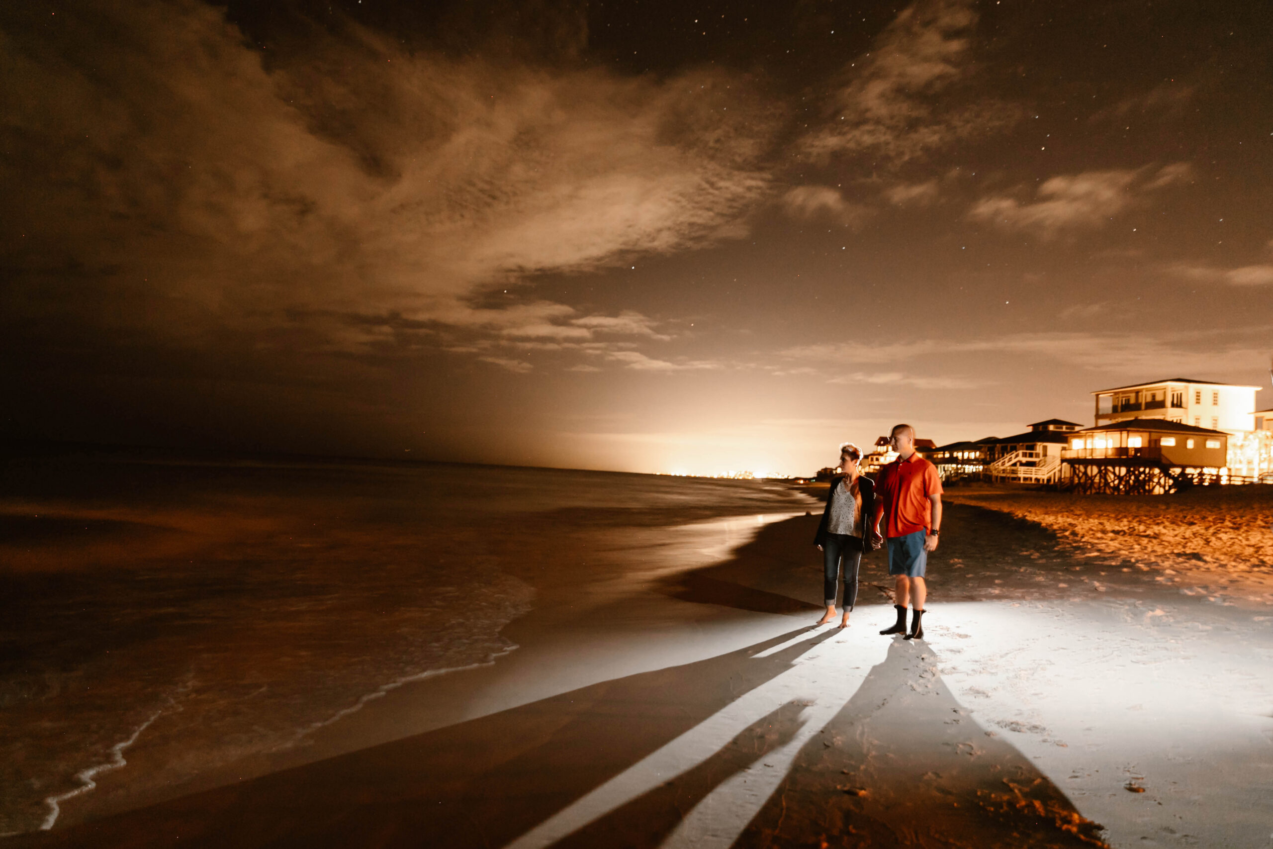 Couple walking the beach at night under a dramatic sky after their Destin vow renewal